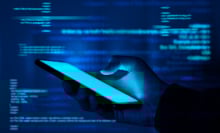 A hand holds a phone in a glowing blue environment filled with floating lines of computer code.
