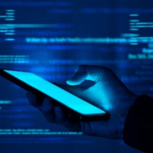 A hand holds a phone in a glowing blue environment filled with floating lines of computer code.